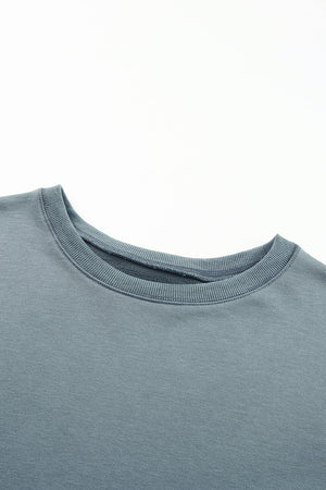 Dull blue crewneck sweatshirt with ribbed collar and cuffs, showing asymmetric hem detail.