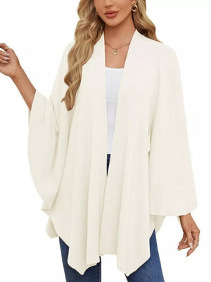 Ivory knit cape top with draped elegance and wide sleeves, worn over a white tank.