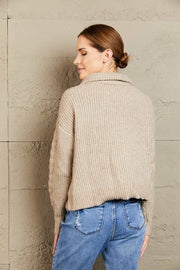 Oatmeal cable knit sweater with a zip-up collar and textured sleeves.