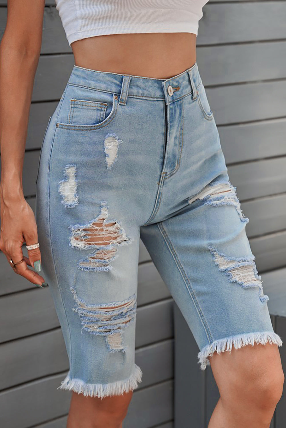 Light wash denim bermuda shorts with distressed rips and frayed hem.