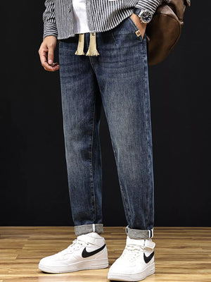 Men's relaxed fit medium wash denim jeans with drawstring and cuffed hems.