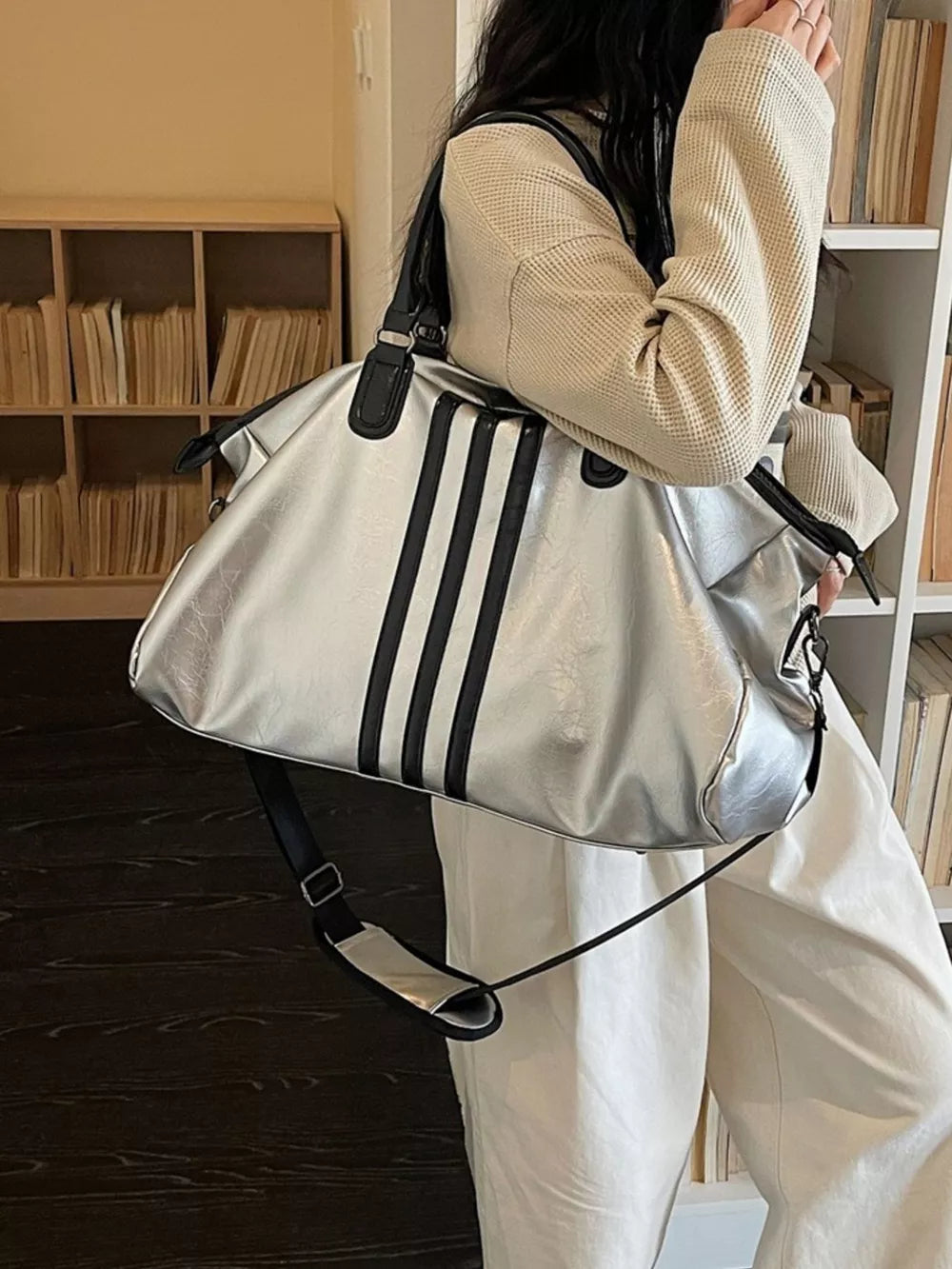 Sleek silver metallic duffle bag with black stripes and black trim, featuring a crossbody strap.
