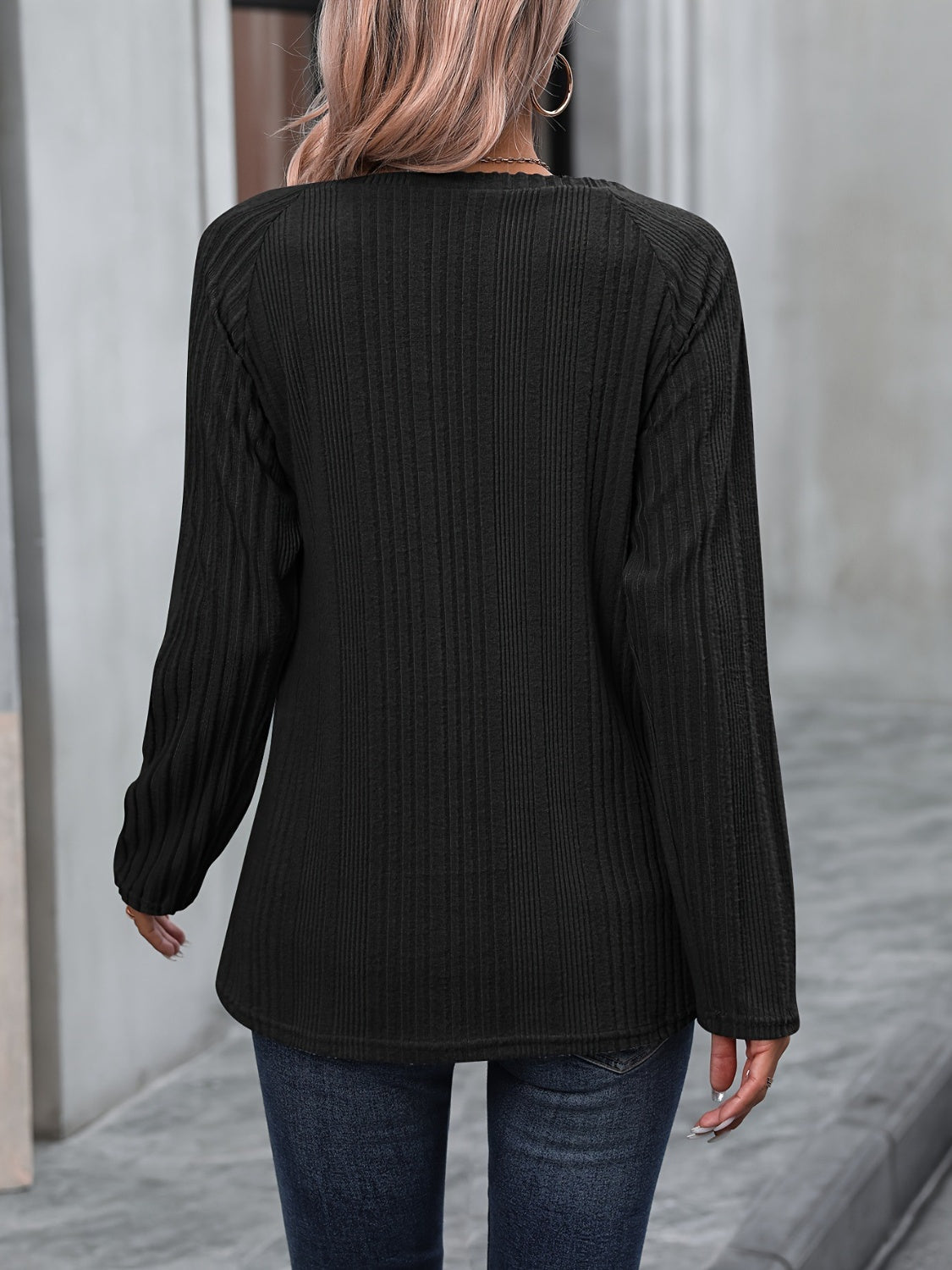Black ribbed knit raglan sweater with long sleeves and button trim detail.
