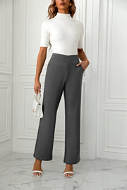 Dark gray wide-leg trousers with a sculpted waist and pockets, styled with a white top and handbag.