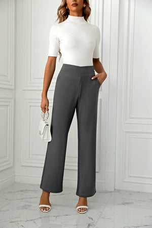 Dark gray wide-leg trousers with a sculpted waist and pockets, styled with a white top and handbag.