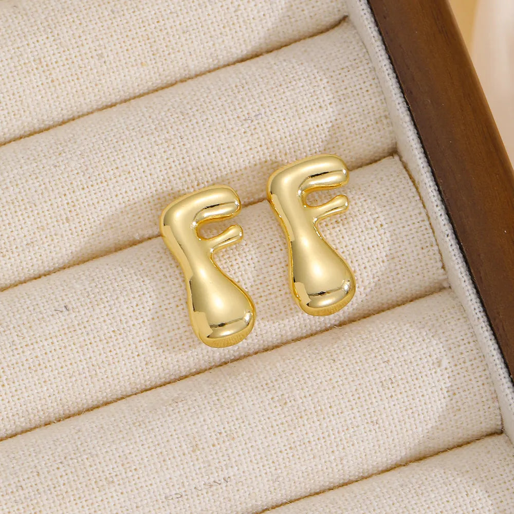 Gold sculptural stud earrings in the shape of the letter F