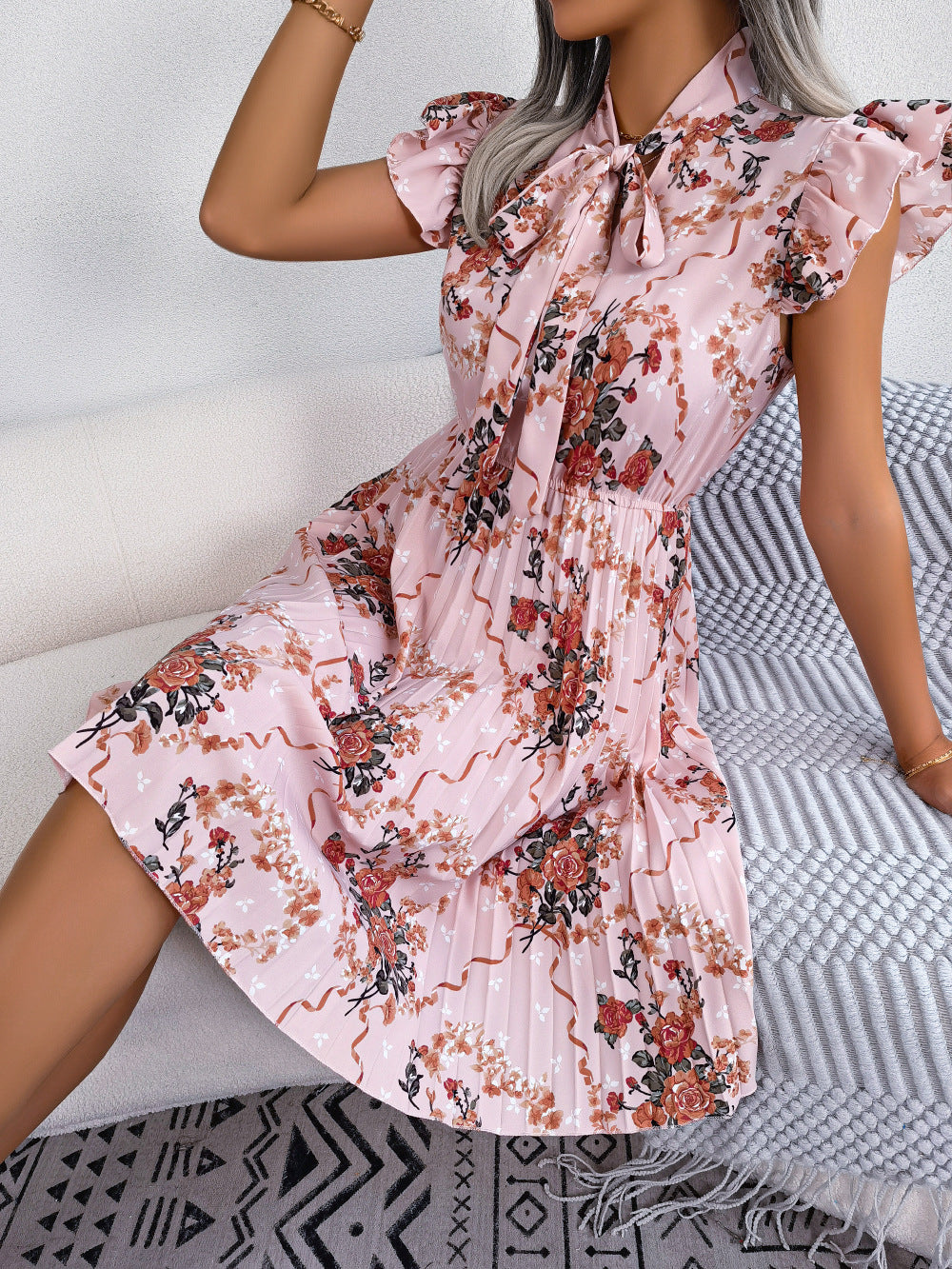 Blush pink floral mini dress with ruffled sleeves, tie neck, and pleated skirt.