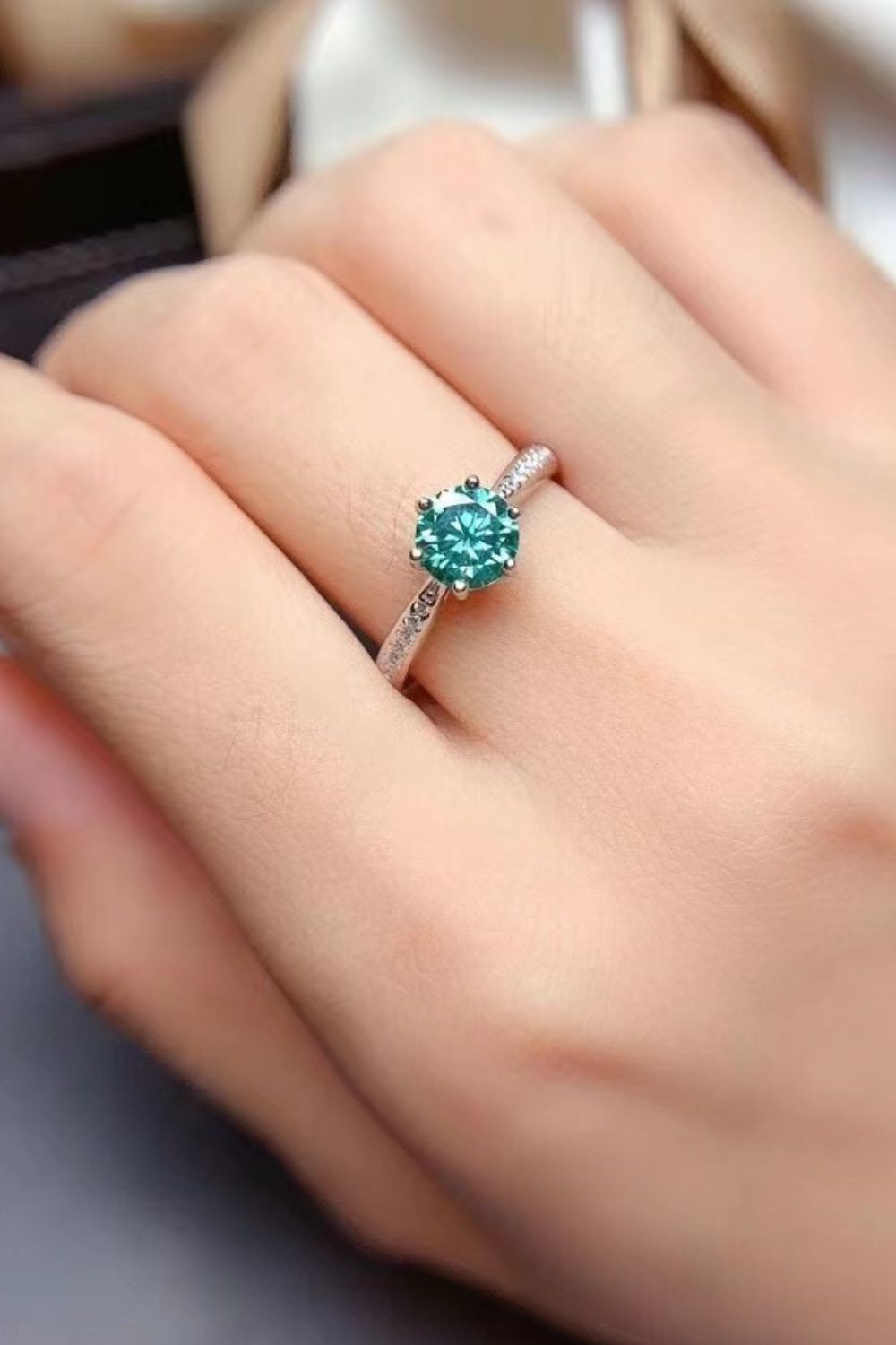 Teal moissanite solitaire ring with pave band on finger