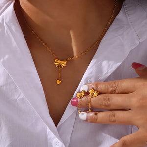 Gold necklace with bow and heart drop pendant, paired with matching bow earrings.