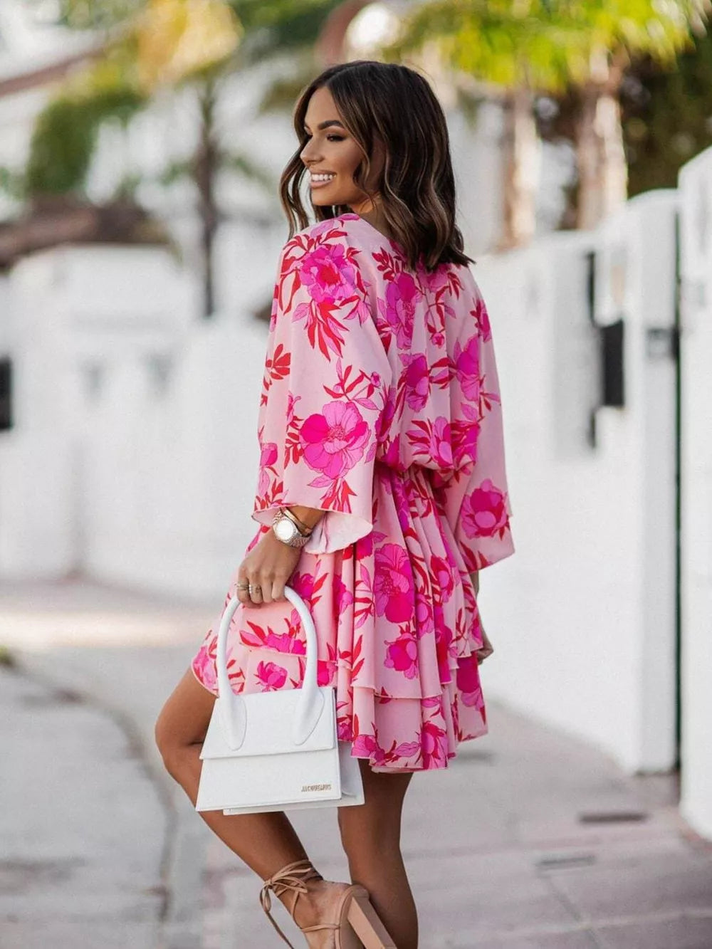 Tropical tiered mini dress in fuchsia pink with floral print, surplice neckline, and ruffled hem.