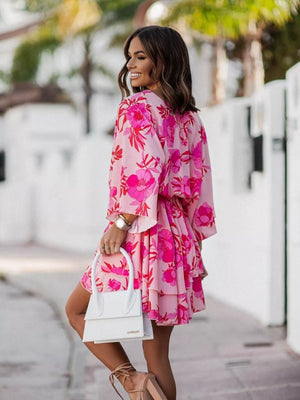Tropical tiered mini dress in fuchsia pink with floral print, surplice neckline, and ruffled hem.
