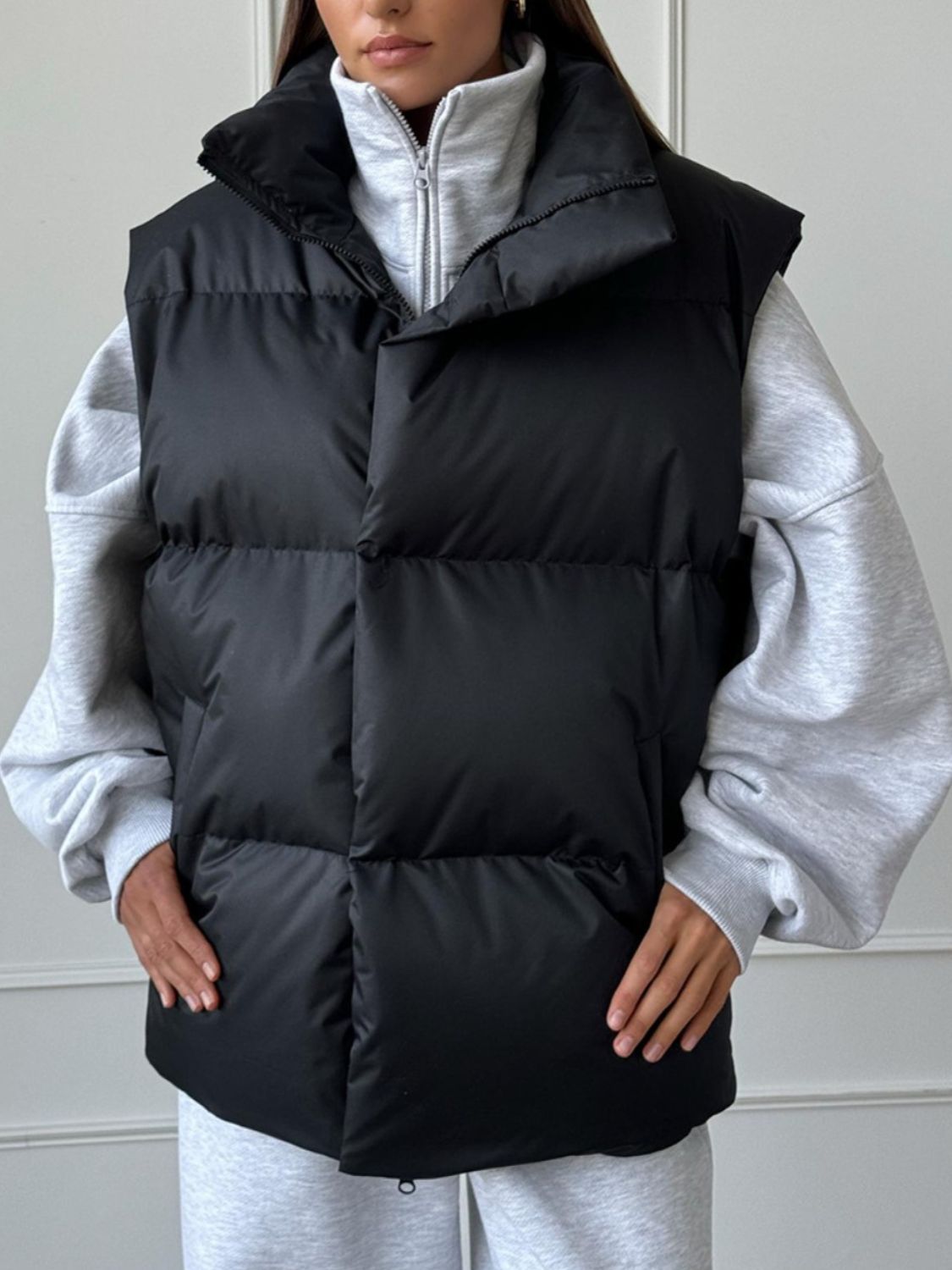 Black padded puffer vest with a high collar, worn over a grey hoodie.