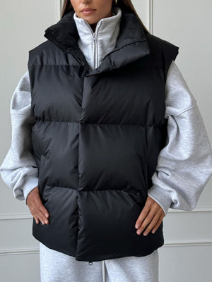 Black padded puffer vest with a high collar, worn over a grey hoodie.