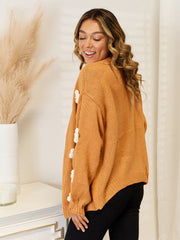 Camel acrylic cardigan with balloon sleeves and white floral embellishments.