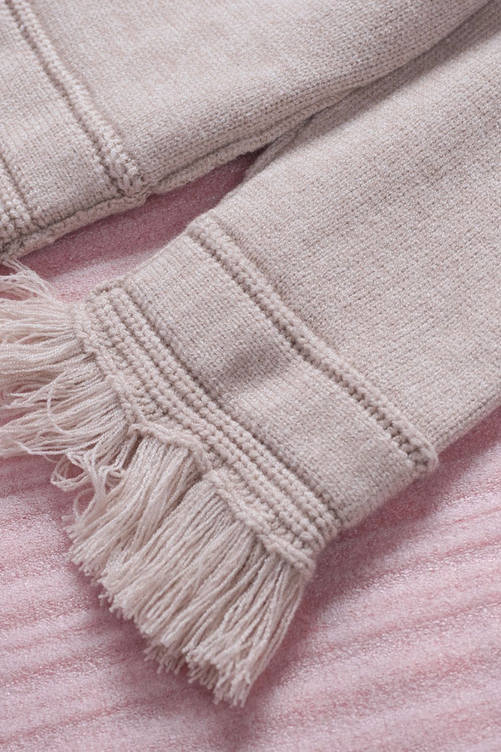 Eggshell knit sweater with off-the-shoulder neckline and fringe trim detail.