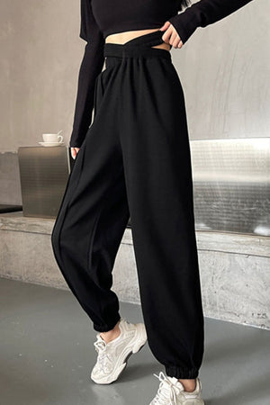 Black pleated waistline joggers with a crossover detail, cuffed ankles, and a relaxed fit.