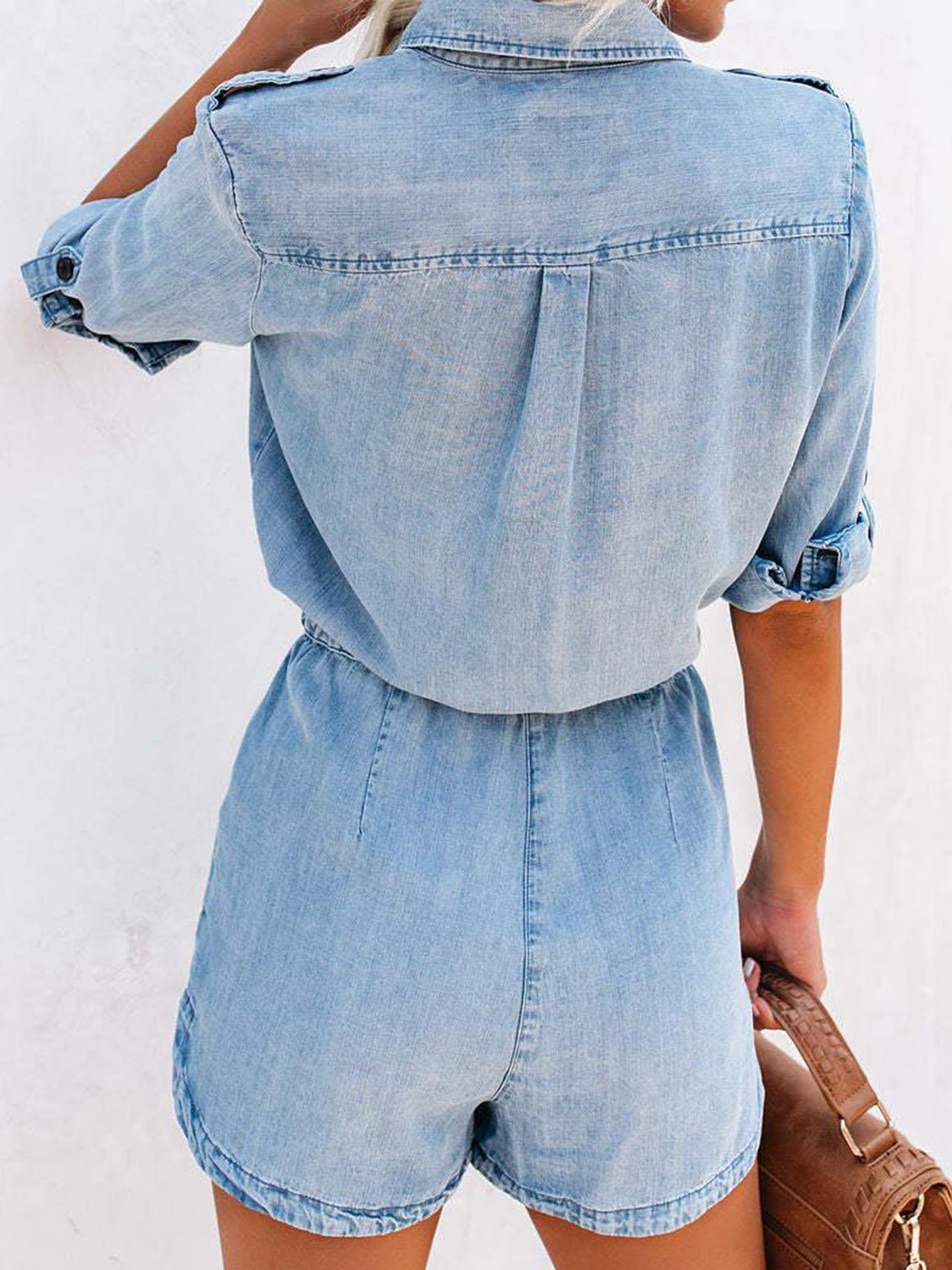 Light wash denim romper with shirred waist and buttoned short sleeves.