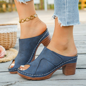 Blue peep-toe block heel mules with perforated detail and white stitching.