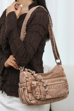 Acid wash denim crossbody bag in camel with multiple zippered pockets and tassel detail.