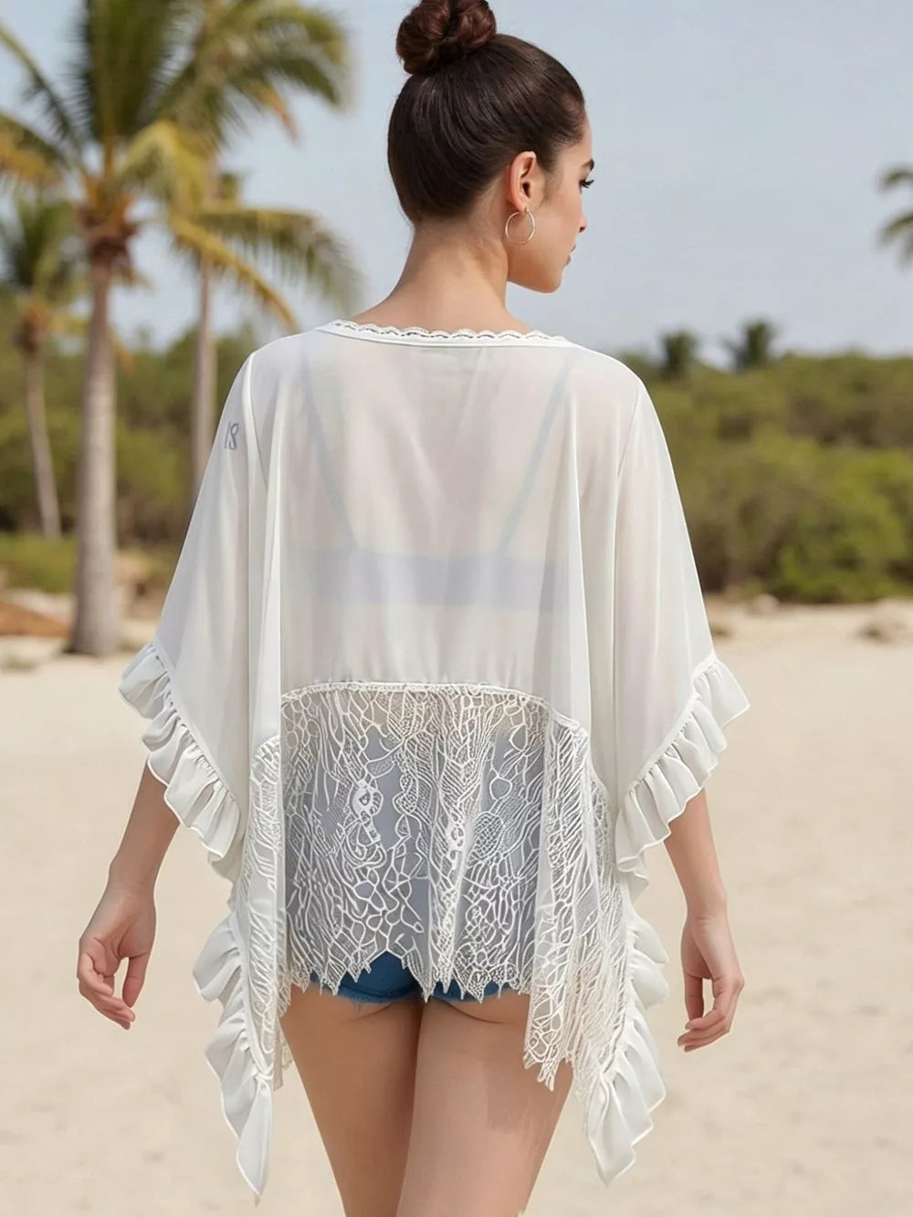 White sheer flowing cover-up with lace trim and ruffled sleeves, worn over denim shorts.