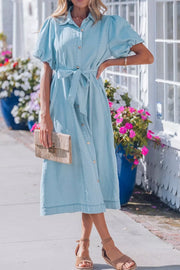 Light blue denim midi dress with puff sleeves, collared neckline, button front, and tie belt.