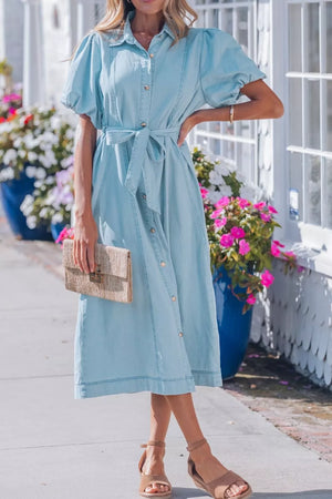 Light blue denim midi dress with puff sleeves, collared neckline, button front, and tie belt.