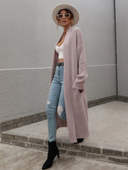 Textured knit maxi cardigan in a soft pink hue with pockets, styled with a white crop top and ripped jeans.