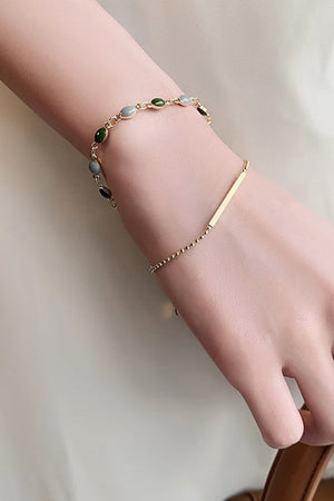 Gold dual chain bracelet with green and gray stones and a bar accent