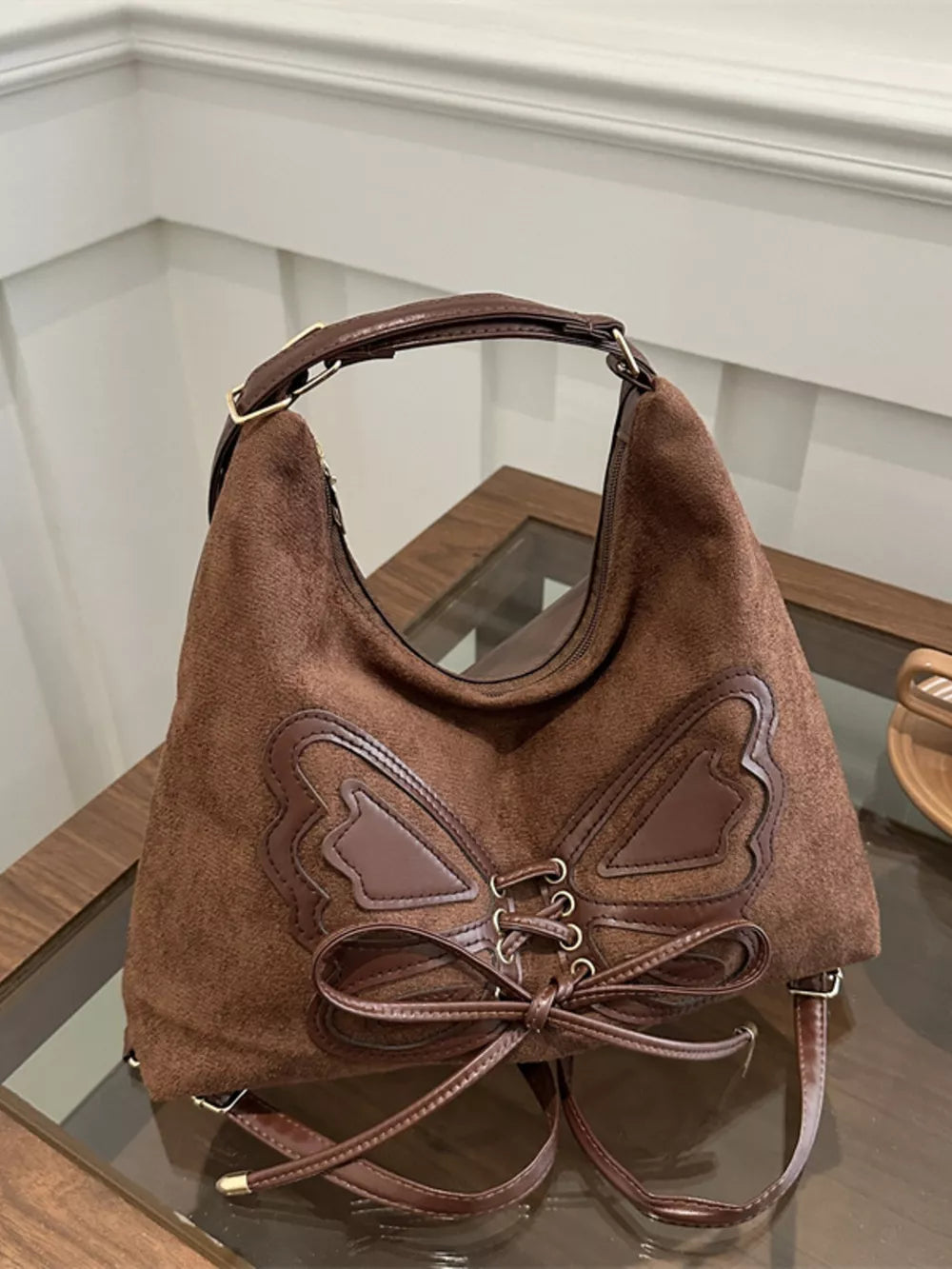 Brown suede half-moon bag with butterfly embellishment and lace-up detail.