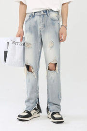 Light wash denim trousers with distressed knee slits and ankle zippers.