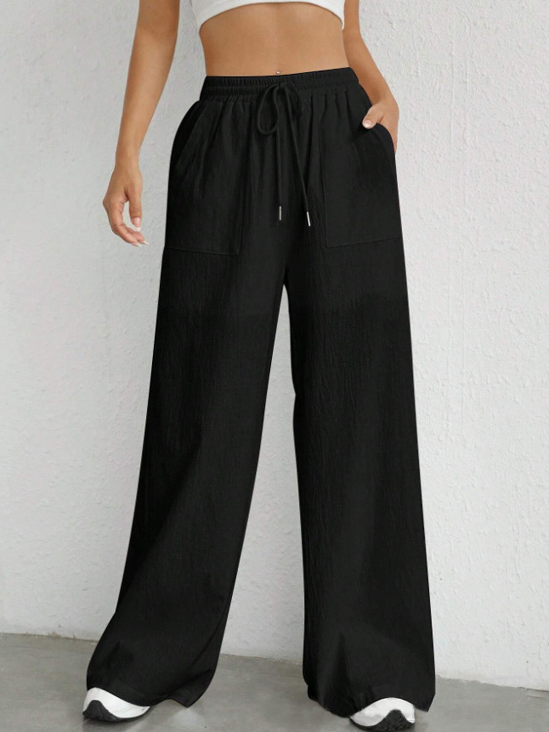 Black linen wide-leg drawstring trousers with pockets and a relaxed fit.
