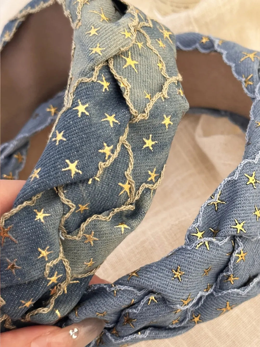 Braided denim headband with gold starburst pattern and scalloped edge detail.