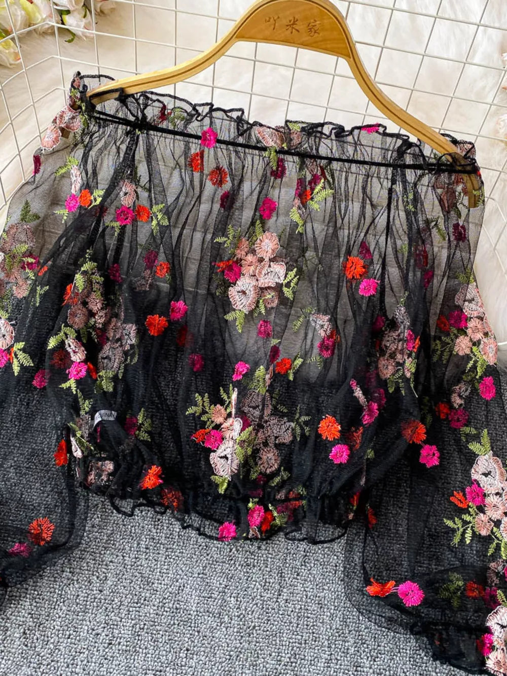 Black off-shoulder t-shirt with colorful floral embroidery and ruffled neckline.