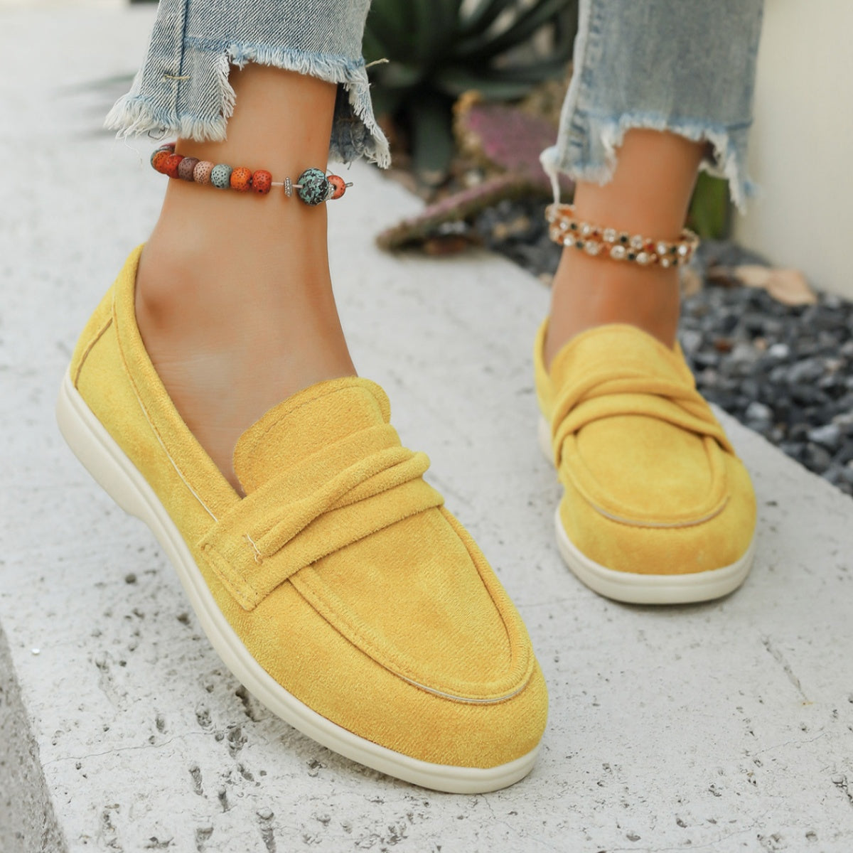 Yellow slip-on loafers with round toe and decorative strap detail.