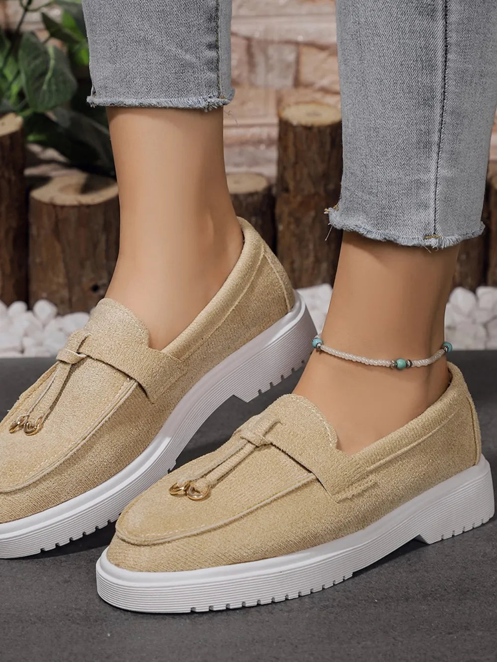 Beige suede loafer slides with tassel detail and gold hardware on white soles.