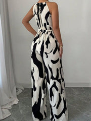 Chic abstract print halter jumpsuit with tie waist and wide legs.