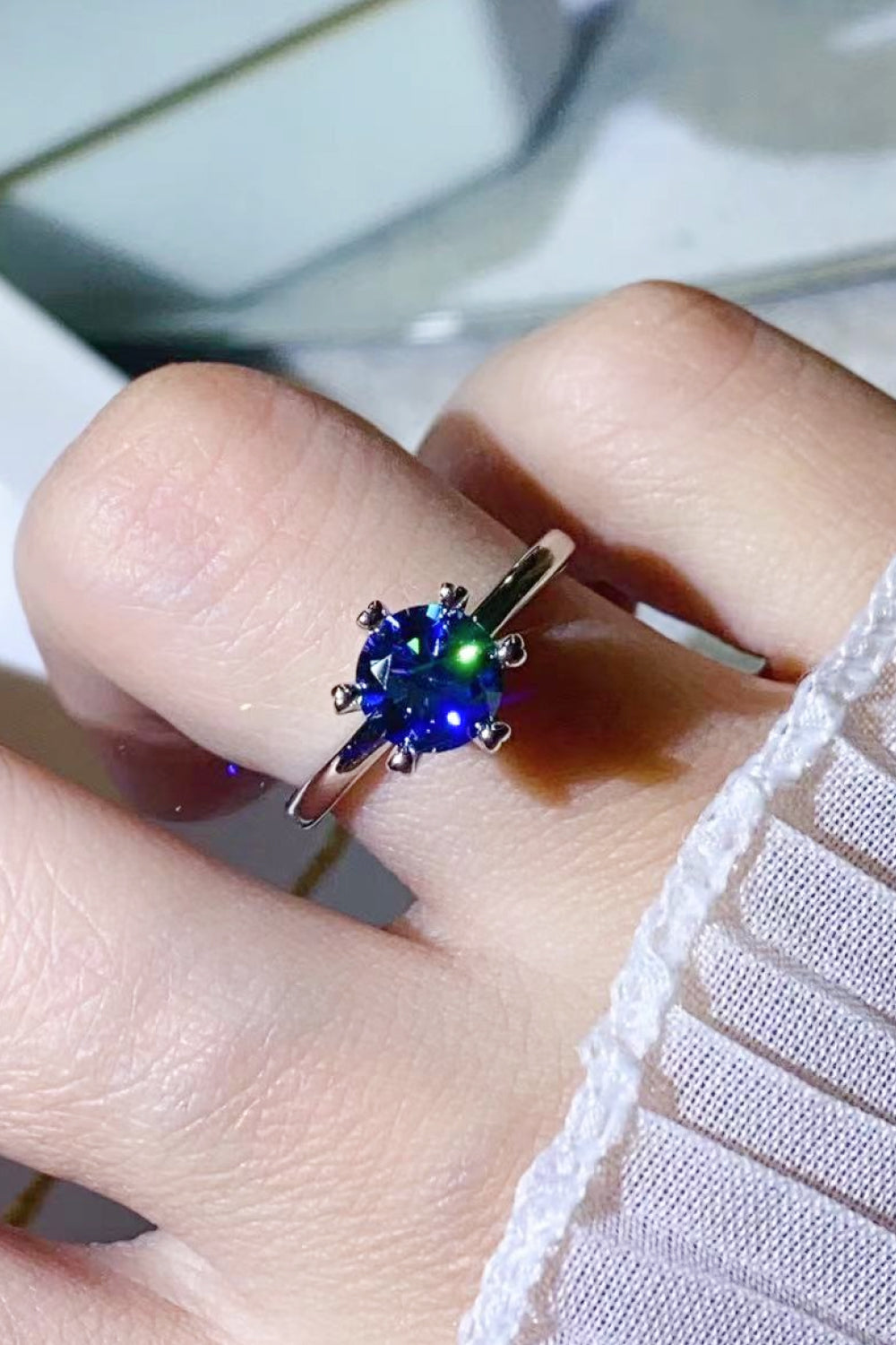 Blue moissanite ring with six-prong setting on a finger