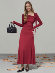 Burgundy ribbed maxi dress with asymmetrical neckline, long sleeves, and tie detail.