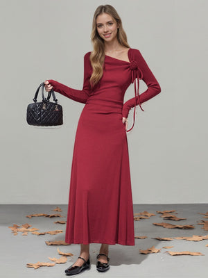 Burgundy ribbed maxi dress with asymmetrical neckline, long sleeves, and tie detail.