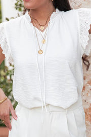 White textured tie-neck blouse with eyelet trim sleeves and ruffled neckline.