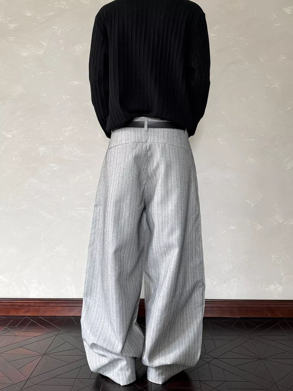 Relaxed wide-leg sweatpants in light gray with subtle vertical pinstripes and a black belt.