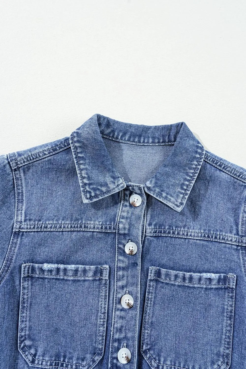 Medium wash denim romper with button-down front and chest pockets.