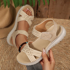 Beige woven strap open-toe flat sandals with adjustable ankle strap and crisscross vamp detail.