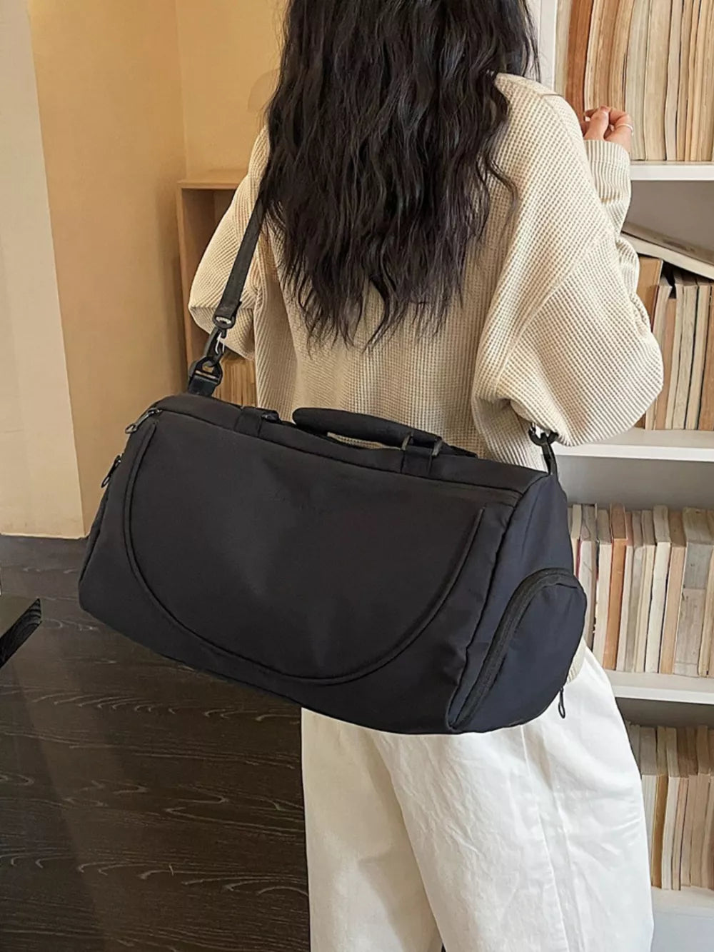 Black medium duffle bag with adjustable strap and side pocket, worn by a person.