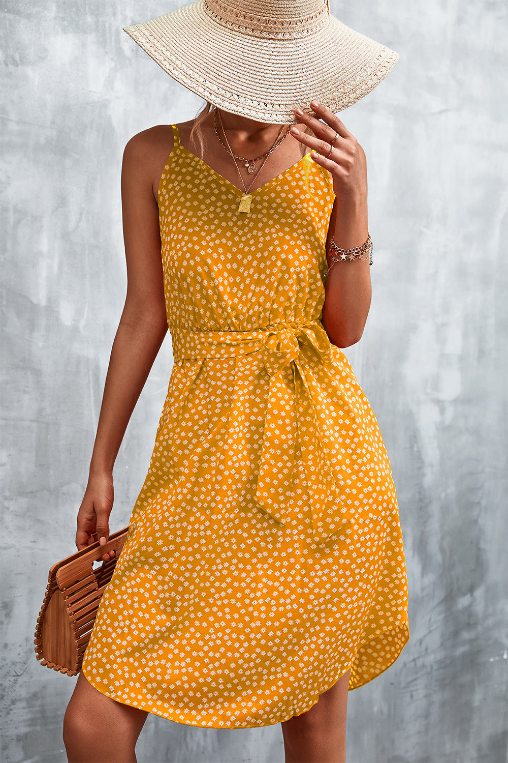 Mustard daisy print slip dress with tie waist and V-neck, styled with a straw hat and bamboo bag.