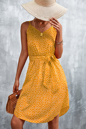 Mustard daisy print slip dress with tie waist and V-neck, styled with a straw hat and bamboo bag.