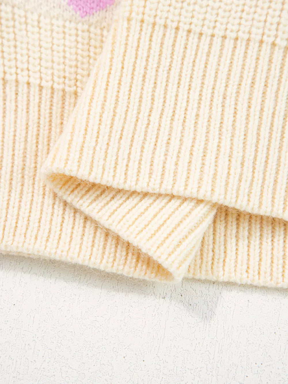 Cream knit sweater with pink heart pattern detail and ribbed cuffs.