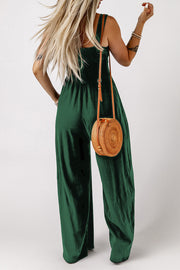 Green smocked square neck wide leg jumpsuit with a round straw bag.