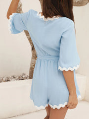Blue linen romper with tie waist and scalloped white trim on sleeves and hem.