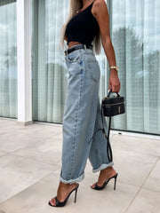 Baggy light wash denim barrel leg jeans with cuffed hems, styled with a black top and heels.